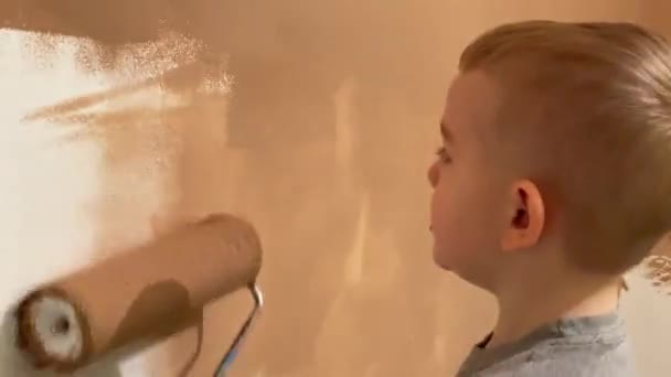 小さな男の子がローラーでテラコッタの彼の部屋に壁を描く — ストック動画