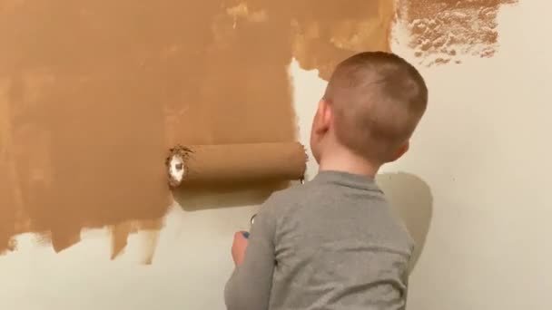 Ein kleiner Junge bemalt in seinem Zimmer eine Wand aus Terrakotta mit einer Walze — Stockvideo