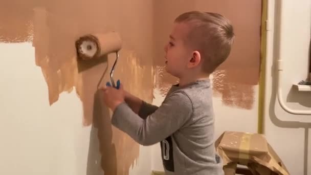 Маленький мальчик рисует стену в своей комнате терракотой с роллером — стоковое видео