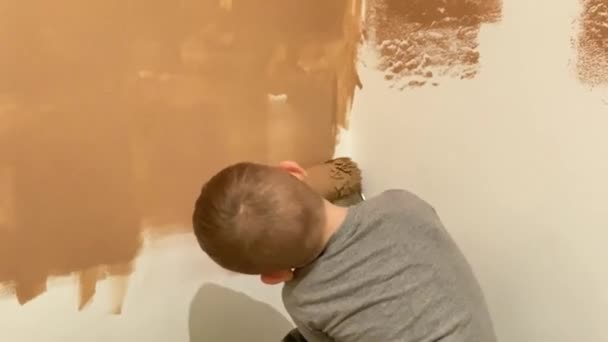 En lille dreng maler en væg i sit værelse i terracotta med en rulle – Stock-video