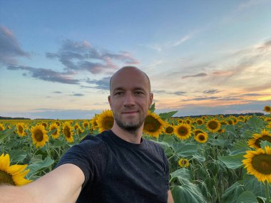 Bir adam Ukrayna 'da çiçek açan ayçiçekleriyle bir tarlada duruyor.