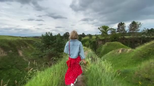Mulher caminhando com um buquê de flores nas colinas verdes — Vídeo de Stock