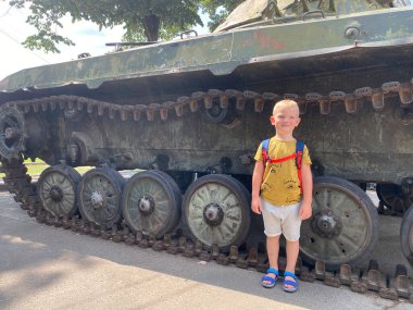 Çocuk Ukrayna, Kyiv 'deki Zafer Parkı' nda bir tankın önünde duruyor.