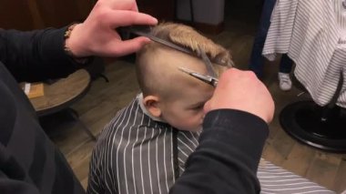 Usta berber dükkanında küçük çocukların saçlarını kesiyor.