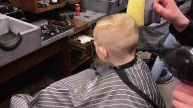 Usta berber dükkanında küçük çocukların saçlarını kesiyor.