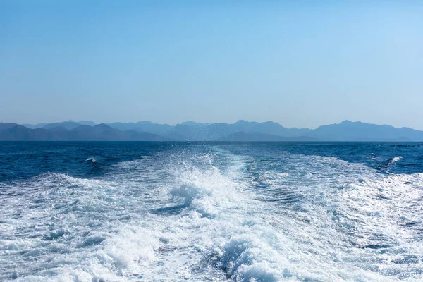 View from a high-speed ship on the blue sea with a mountainous coast in the background Stock Photo