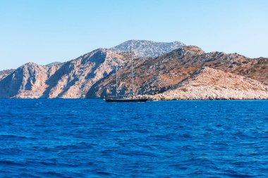 Yunanistan 'dan geçen bir gemiden adanın manzarası. Yat kayalık bir ada denizinin arka planında yüzüyor..