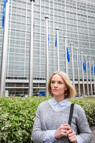 Young woman in casual clothes stands against the backdrop of the European Commission headquarters in Brussels, Belgium