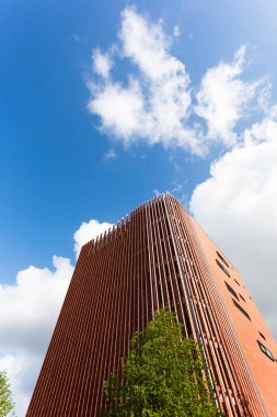 Ön cephesinde parlak terracotta dikey levhaları olan modern bir bina. Modern mimari