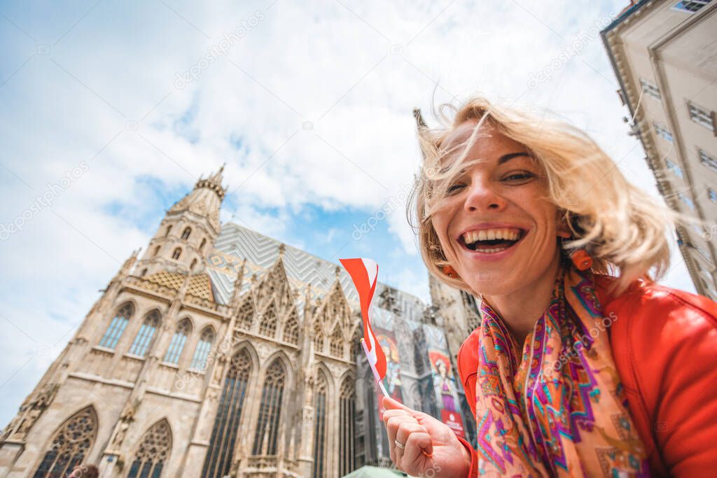 Young beautiful smiling woman in a red jacket with the flag of Austria in hand stands on the background of St. Stephens Cathedral in Vienna , Austria