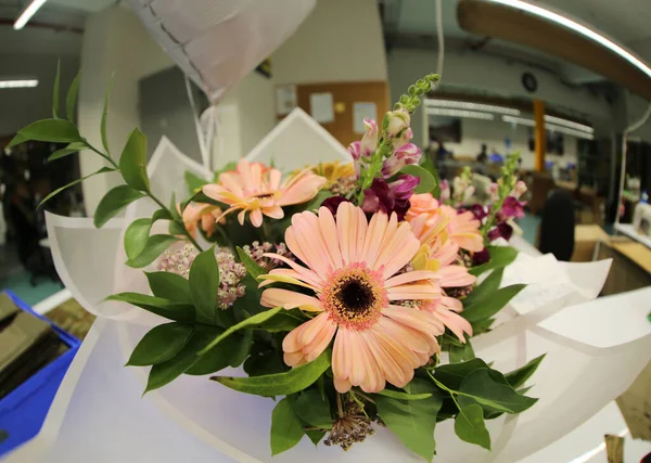a beautiful gift bouquet in white packaging stands on a table in a vase