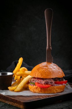 Siyah angus biftekli domates, marul ve patates kızartmalı hamburger. Bıçak topuza saplanmış.