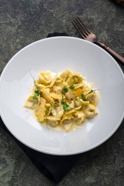 Beyaz tabakta ördek, kızarmış ekmek ve peynir soslu Tortellini.