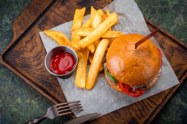 Orta boy biftek, domates ve marullu hamburger. Tahta üzerinde patates kızartması olan yemek seti, üst manzara.