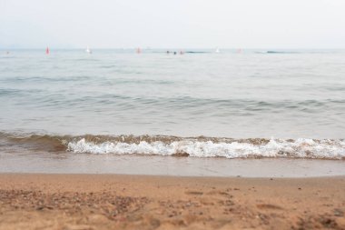 Pastel mavi dalgalar yazın kumlu bir sahilde yıkanır.