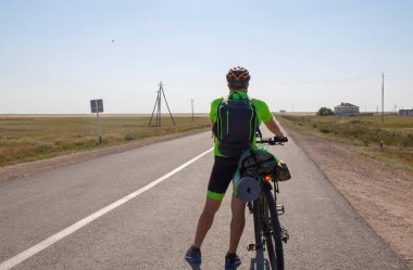 Bicycle tourist looking forward, standing on an empty road