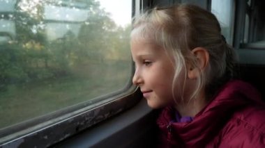 Kız düşünceli bir şekilde tren penceresinden dışarı bakıyor. Güneş ışınları, yüzü aydınlatır. Eski tren ortalama bir hızla hareket eder.