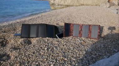 Zaman aşımı. İki güneş paneli, deniz kenarındaki taştan bir plajda güneşten elektrik çeker ve telefonunuzu ve akıllı telefonunuzu şarj eder. Alternatif enerji..