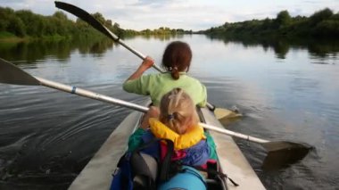 Anne ve kızı sakin bir nehirde kanoyla kürek çekiyorlar. Suda aktif yaz tatili. Can yeleği giyen kız..