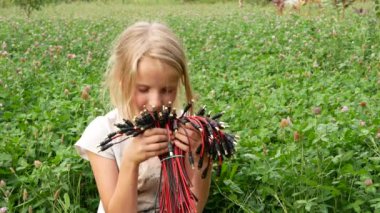 A girl sniffs a bouquet of plastic connectors. A field of flowers.