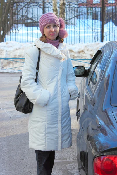 Una mujer con un abrigo blanco de pie cerca del coche — Foto de Stock