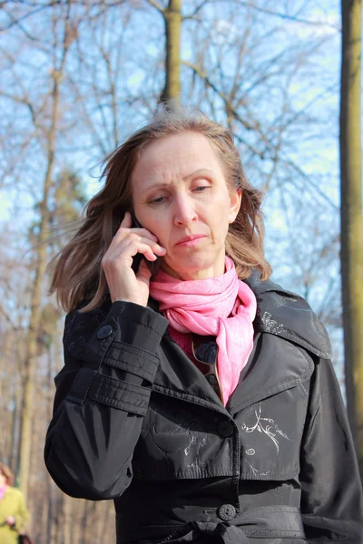 Una mujer con un abrigo negro hablando en un teléfono móvil — Foto de Stock