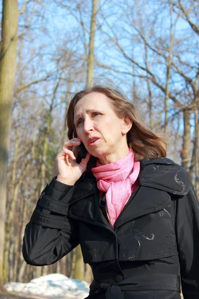 Una mujer con un abrigo negro hablando en un teléfono móvil — Foto de Stock