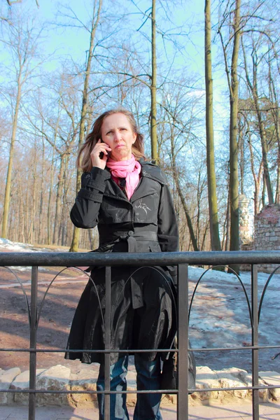 Una mujer con un abrigo negro hablando en un teléfono móvil — Foto de Stock