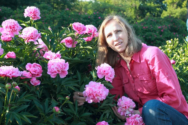 Vrouw in de buurt van een bush pioenrozen — Stockfoto