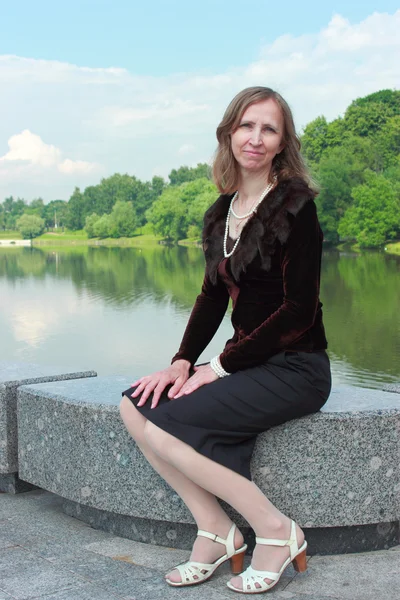 En kvinna sitter på räcket nära dammen — Stockfoto