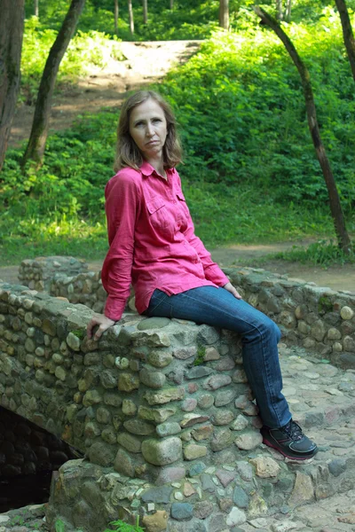 Una mujer sentada en un parapeto de puente de piedra — Foto de Stock