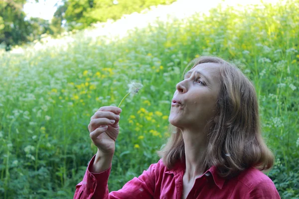 Femme soufflant sur un pissenlit — Photo