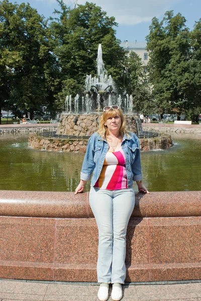 Una mujer se para cerca de una fuente — Foto de Stock