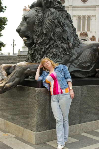 A woman stands near a sculpture of a lion — Stock Photo, Image