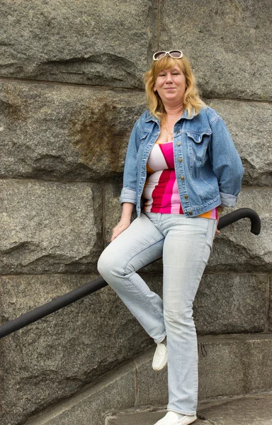 Een vrouw in een blauwe jas staande in de buurt van een stenen muur — Stockfoto