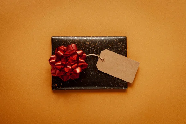 黄色の背景に赤い弓で暗い贈り物 トップビュー — ストック写真