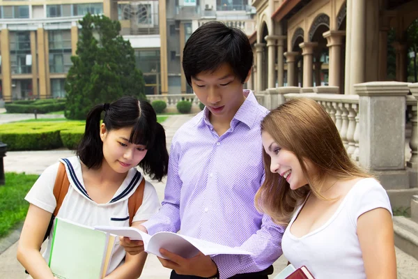 Group of young students look at book and talk — Stock Photo, Image