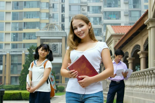 Νεαρή κοπέλα κρατώντας το βιβλίο και να χαμογελά. ομάδα μελέτης φοιτητές — Φωτογραφία Αρχείου
