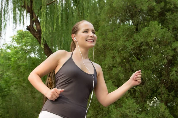 Beautiful young woman running in green park on summer day — Stock Photo, Image