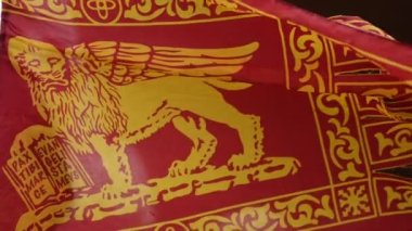 Rüzgarda dalgalanan Venedik bayrağı, çok güçlü bir kimlik ve aidiyet sembolü, kanatlı bir aslan tasvir ediyor, şehrin koruyucu azizi ve Venedik Serenissima Cumhuriyeti 'nin sembolü.