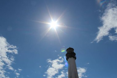 Güneş gökyüzündeki beyaz bir fenerin arkasında parlıyor.