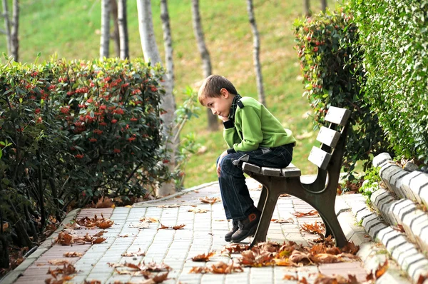 Menino triste sentado sozinho em um banco de certa forma — Fotografia de Stock