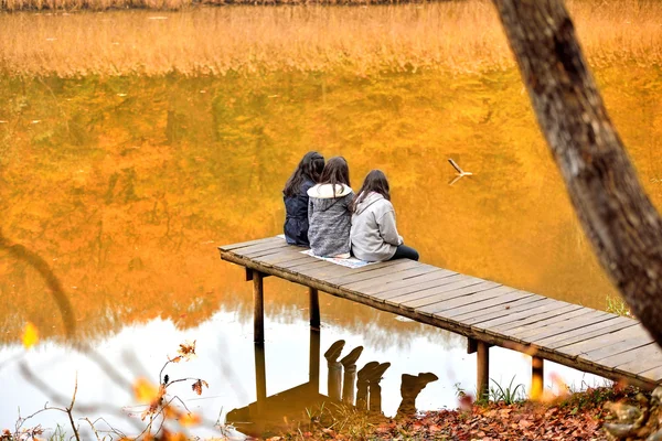Com três meninas sentadas na ponte de madeira no cenário de outono — Fotografia de Stock