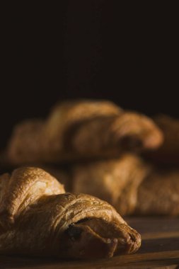 Baked fresh croissants with chocolate in the kitchen interior on a wooden dividing board on a dark background. Photos of food for cafes, restaurants, home kitchens and other culinary topics.