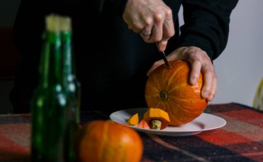 Cadılar Bayramı kutlaması için balkabağı oyan erkek eller yeşil cam şişelerde mumların yanında kareli bir battaniye ile.