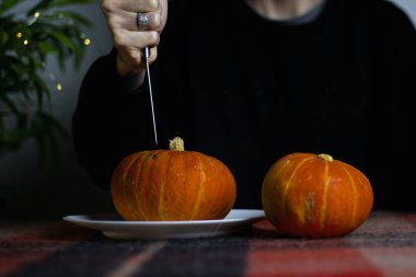 Sonbahar Cadılar Bayramı Balkabağı Erkek Ellerinde Siyah bir kazakla mutfak bıçağıyla kareli ekoseli bir masada beyaz bir tabakta tatile hazırlanıyor.. 