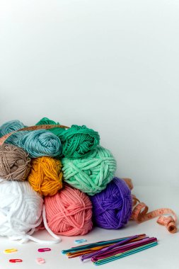 Beyaz arka planda farklı çapta çok renkli örgü kancaları, iplik izleri ve turuncu santimetre şeritlerin yanında. Yatay bir arkaplanda. Hobi, el yapımı, el işi.