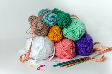 Beyaz arka planda farklı çapta çok renkli örgü kancaları, iplik izleri ve turuncu santimetre şeritlerin yanında. Yatay bir arkaplanda. Hobi, el yapımı, el işi.