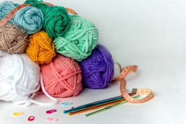 Beyaz arka planda farklı çapta çok renkli örgü kancaları, iplik izleri ve turuncu santimetre şeritlerin yanında. Yatay bir arkaplanda. Hobi, el yapımı, el işi.