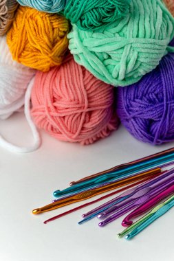 Beyaz arka planda farklı çapta çok renkli örgü kancaları, iplik izleri ve turuncu santimetre şeritlerin yanında. Yatay bir arkaplanda. Hobi, el yapımı, el işi.